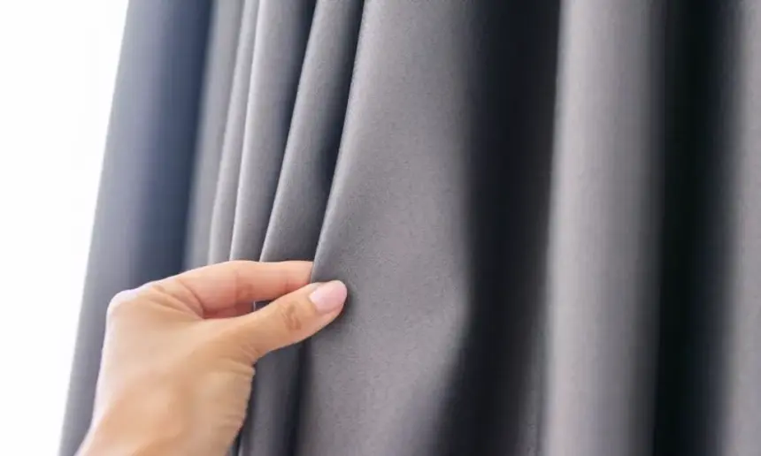 A hand touches a blackout curtain.