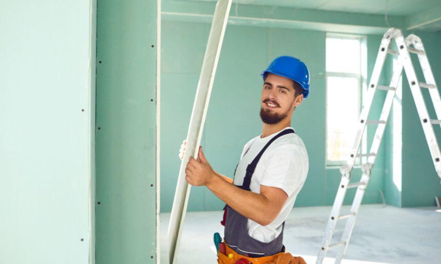 Construction worker installs plasterboard drywall.