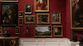 A red wall with a number of art paintings.